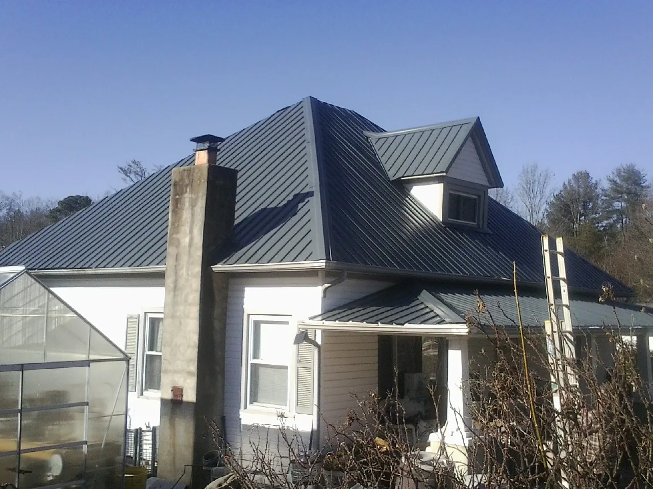 Dark blue standing seam metal roof on a white farmhouse with dormer — Slate & Tile Roof Repair by Roofing Brothers in Okarche