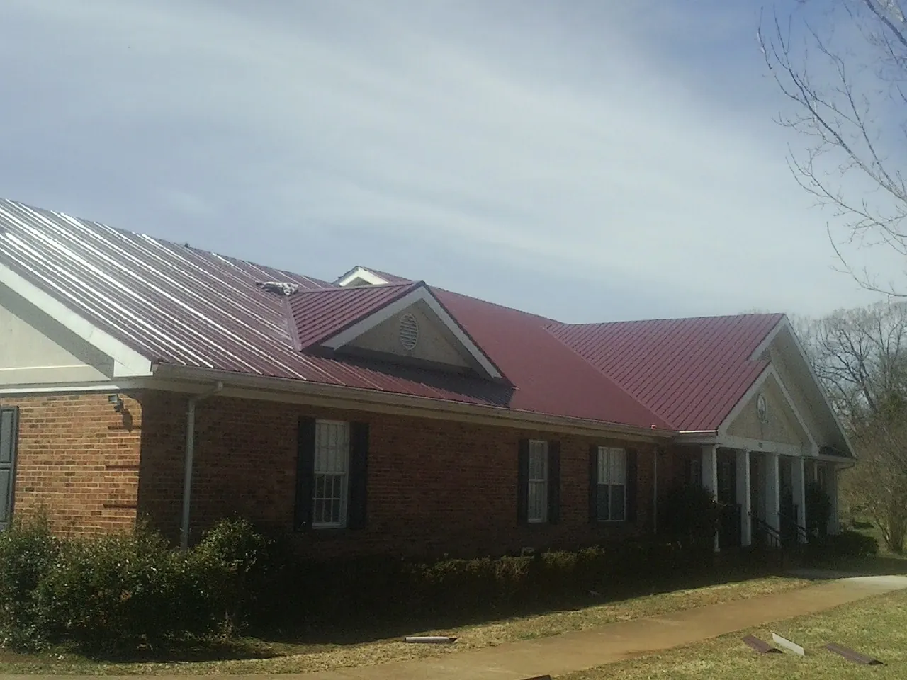 Red metal roof with gabled entries on a long brick building, from a Hail Damage Roof Repair job in Okarche