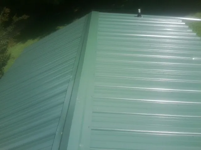 New green metal panels meeting at the ridge of a roof — Flat Roof Repair work by our crew in Okarche