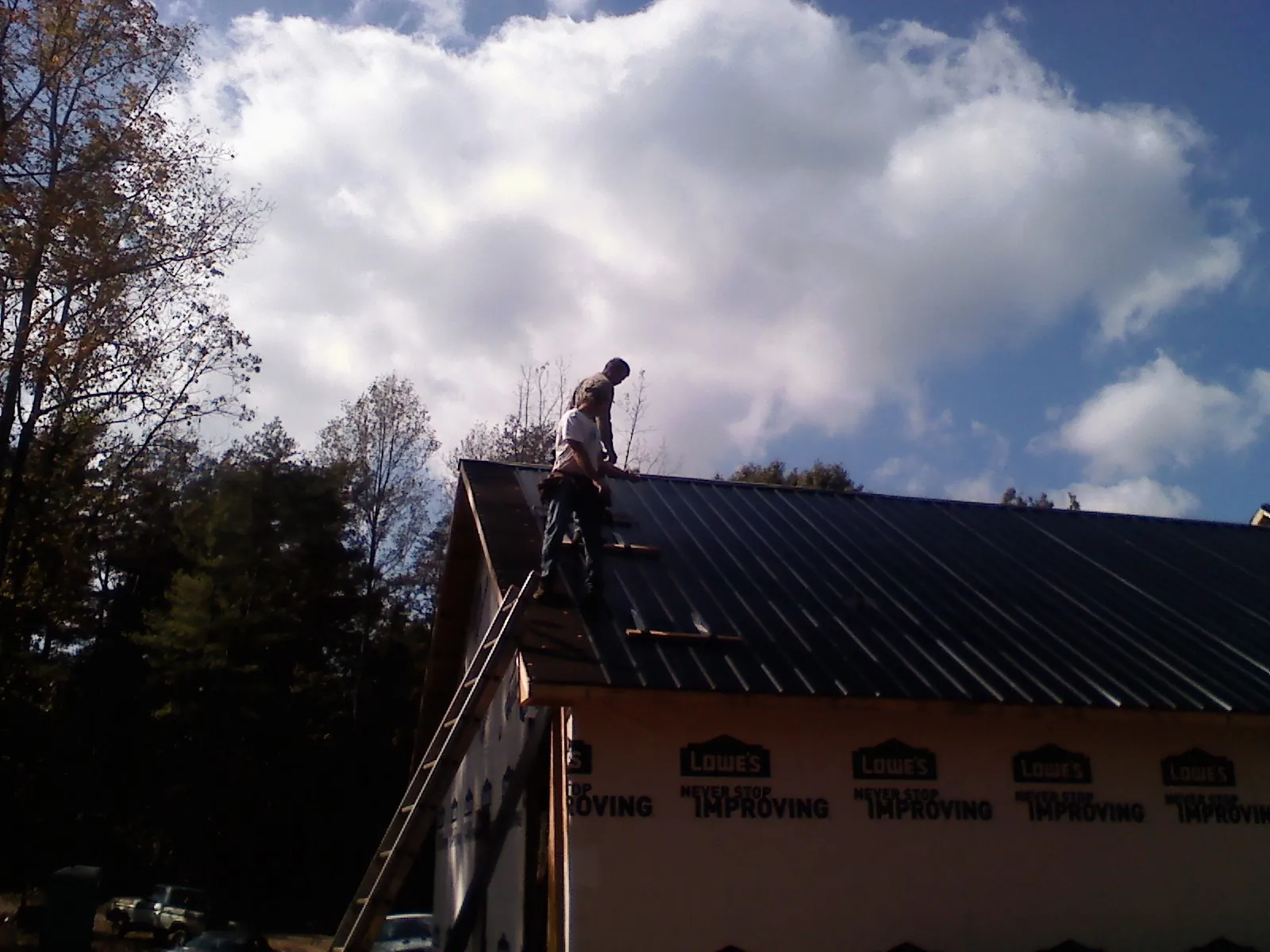 Roofer fastening dark metal panels high against a cloudy sky, from a Roof Inspection job in Okarche