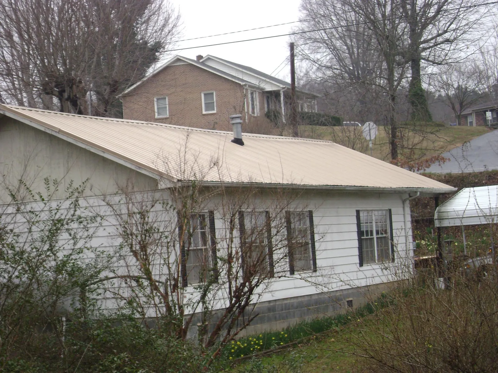 Tan metal roof on a white sided house set into a hillside — Commercial Roofing by Roofing Brothers in Okarche