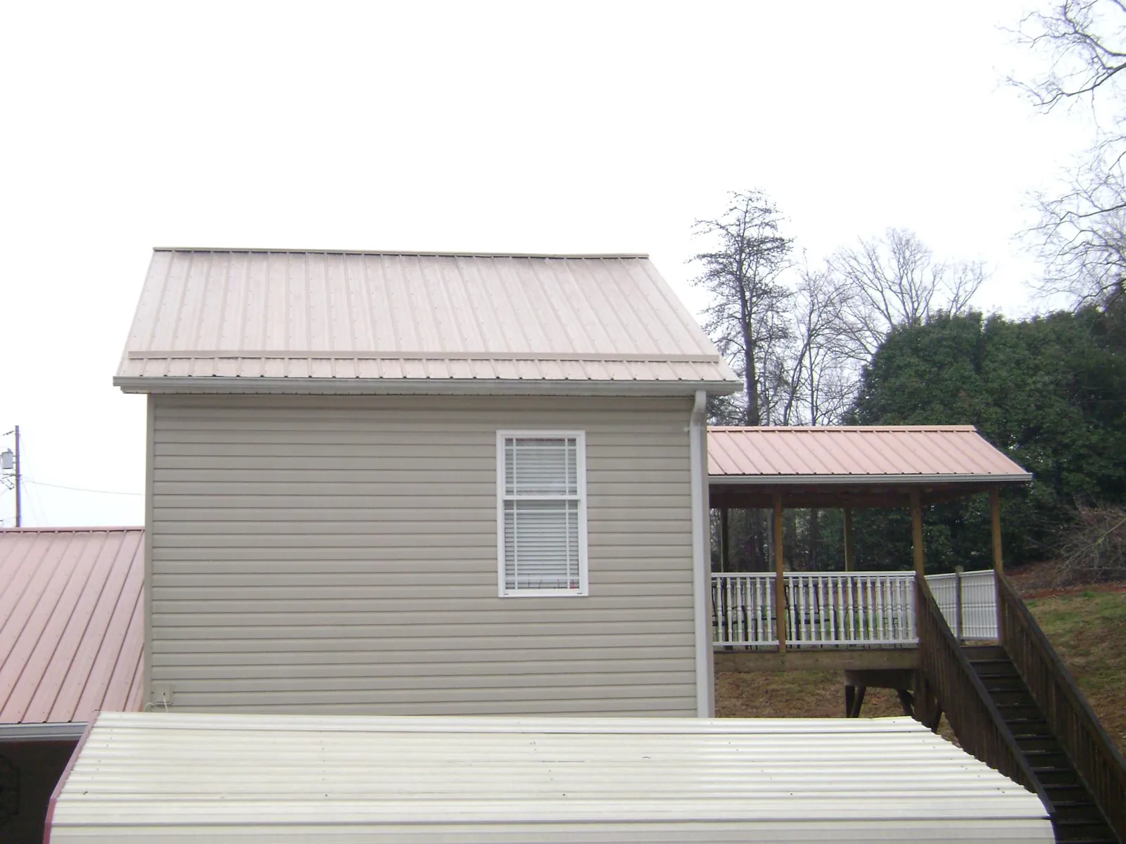 Tan metal roofs on a two story addition and attached porch, from a Roof Replacement job in Okarche